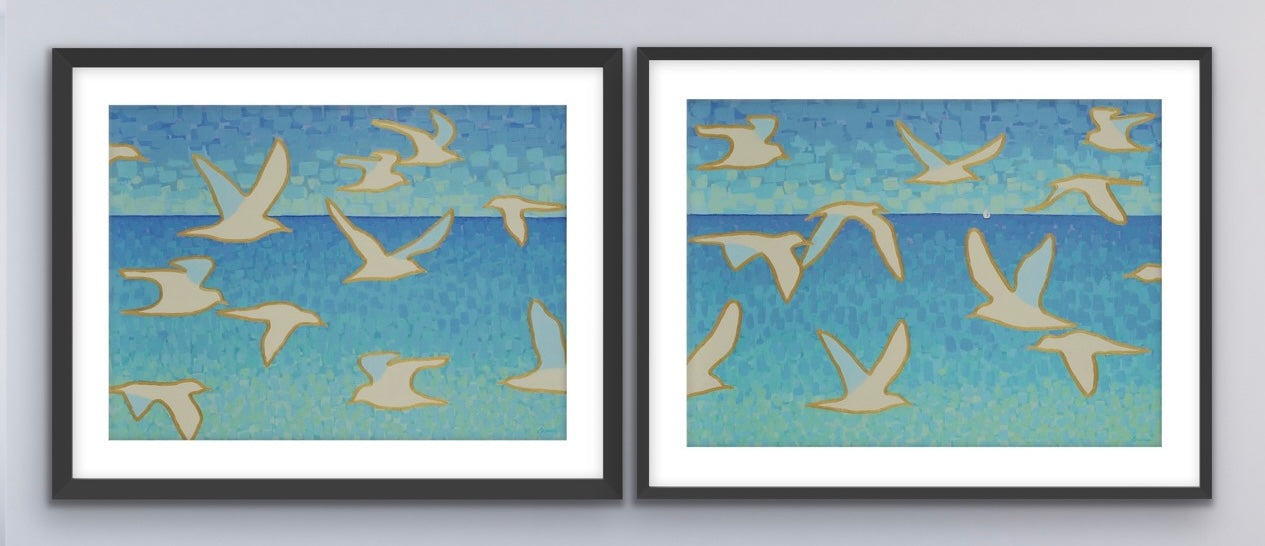 Two oceanview framed artworks of birds flying against a blue sky on a gray wall.