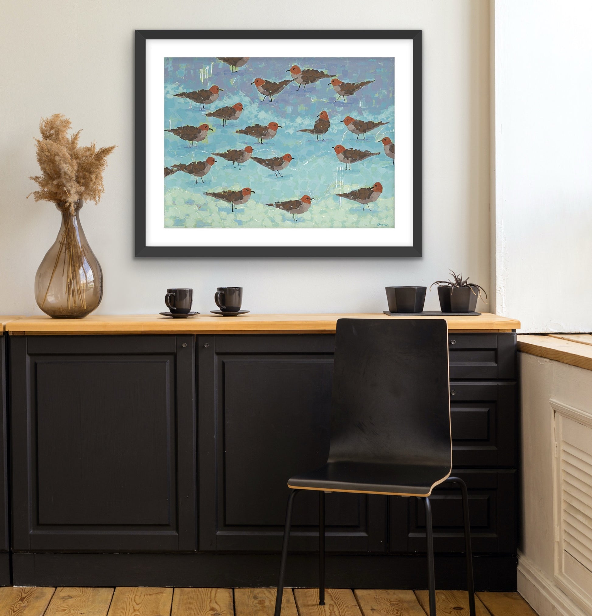 Ocean-inspired fine art print capturing the calm beauty of seagulls by the shore on a wall above a kitchen counter with black chairs.