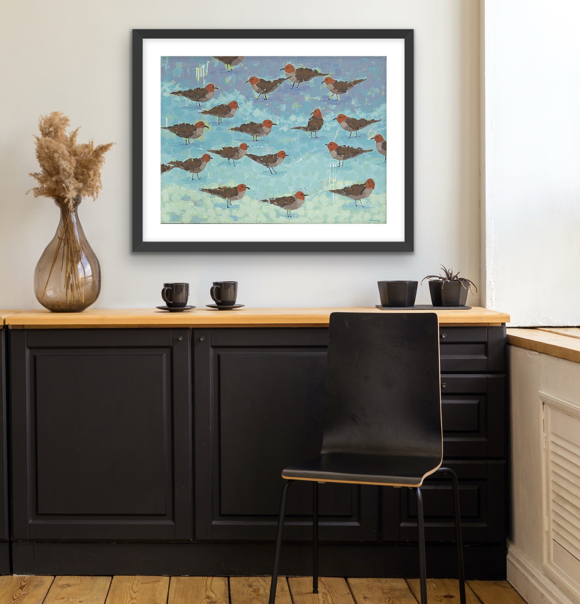 Ocean-inspired fine art print capturing the calm beauty of seagulls by the shore on a wall above a kitchen counter with black chairs.