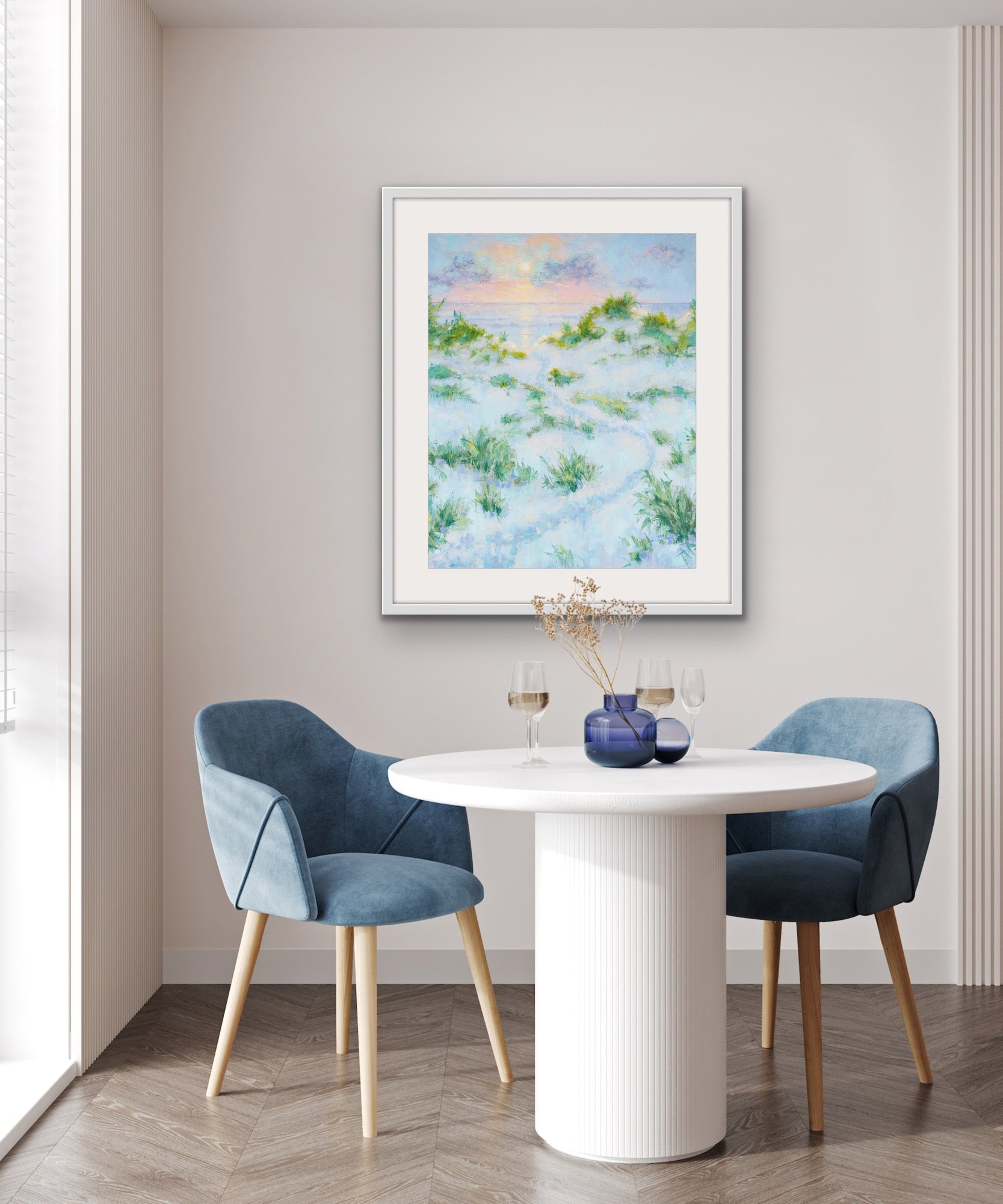Dining room with a white round table and blue chairs, featuring a vertical dune path landscape printed on archival cotton rag print on the wall.