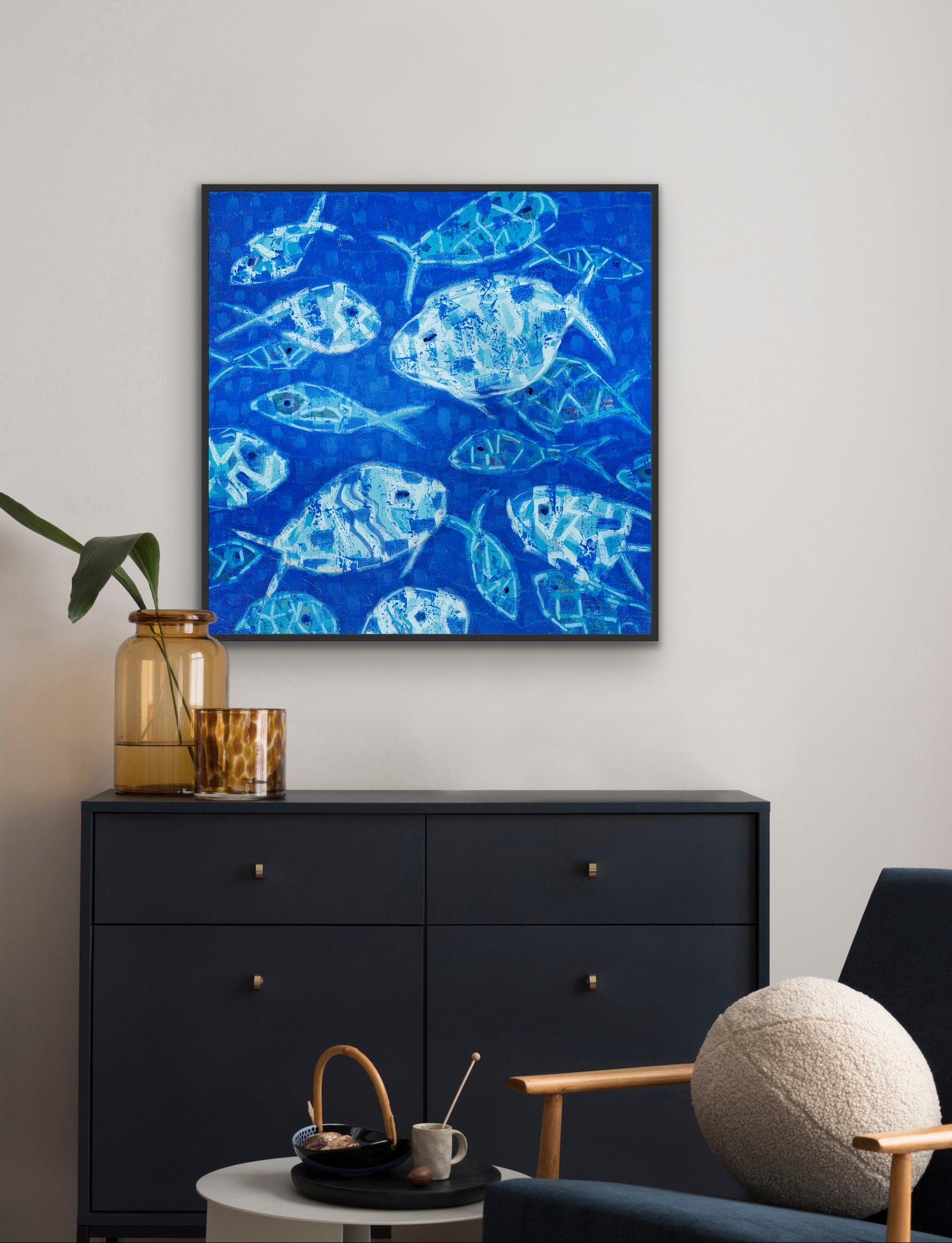 Contemporary ocean-themed wall art in cobalt and aqua tones on a wall above a black cabinet with a blue chair and decorative items.