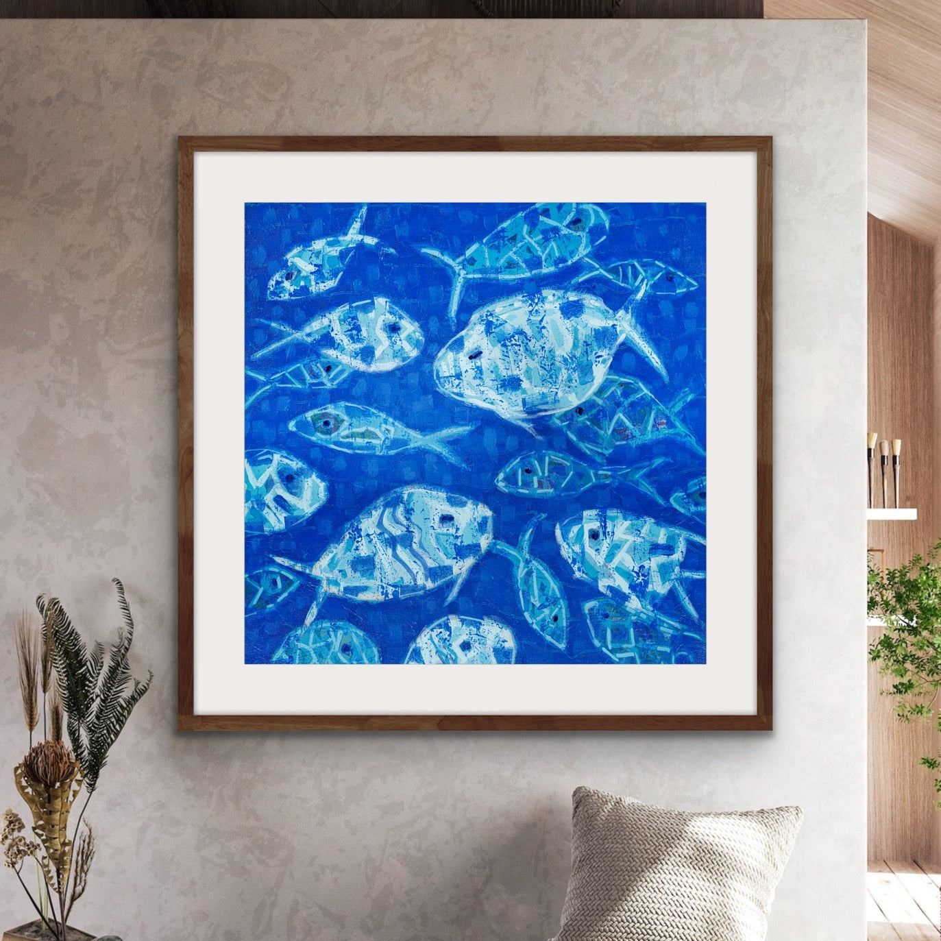 Modern square coastal artwork with fish in cobalt blue tones on a wall in a modern living room.