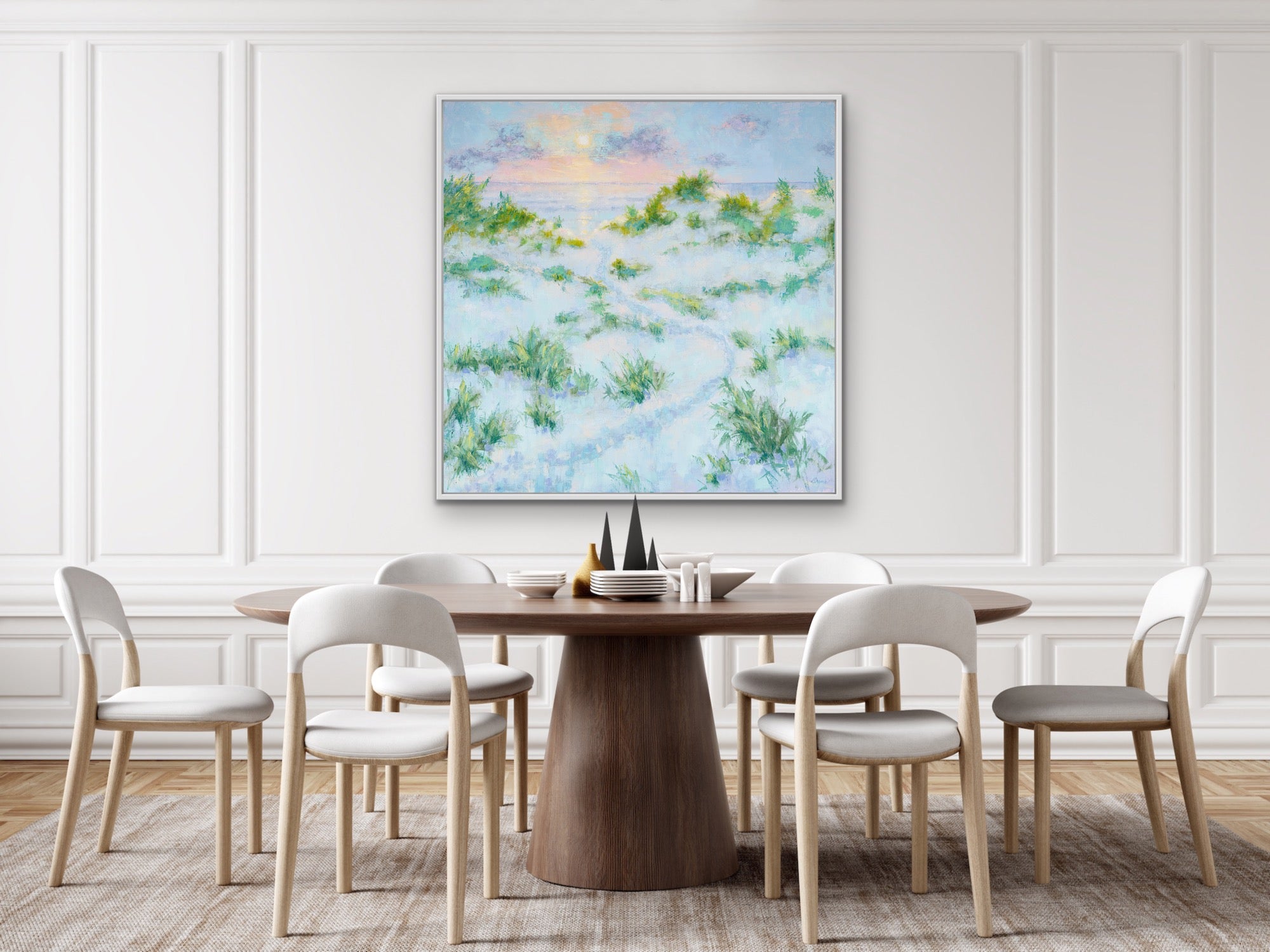 Dining room with a round wooden table and chairs, and a large framed elegant beach sunrsie landscape painting on the wall.