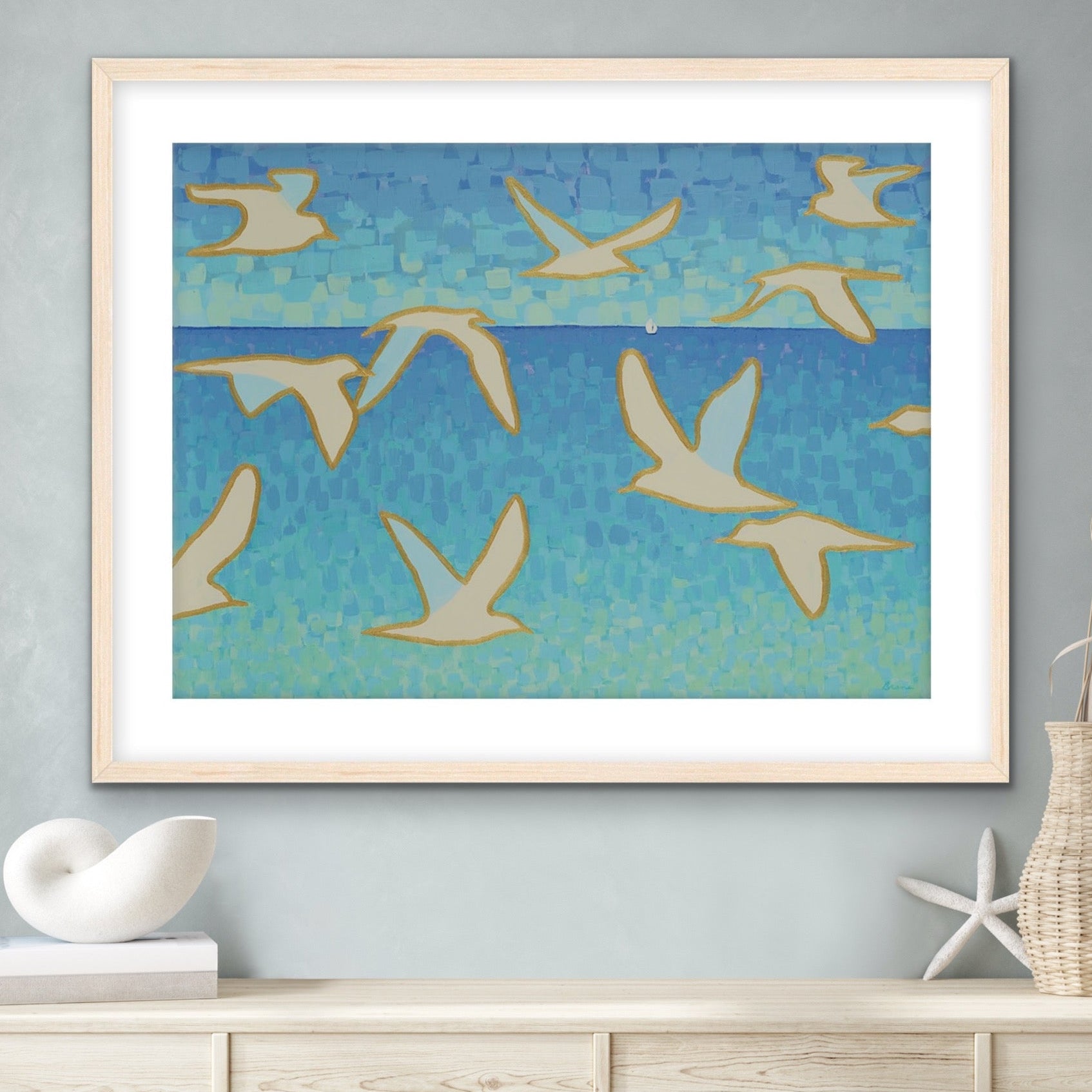 Wings of Light II giclée canvas print with white seagulls over soft ocean blues, modern luxury coastal wall art above a cabinet with coastal objects.