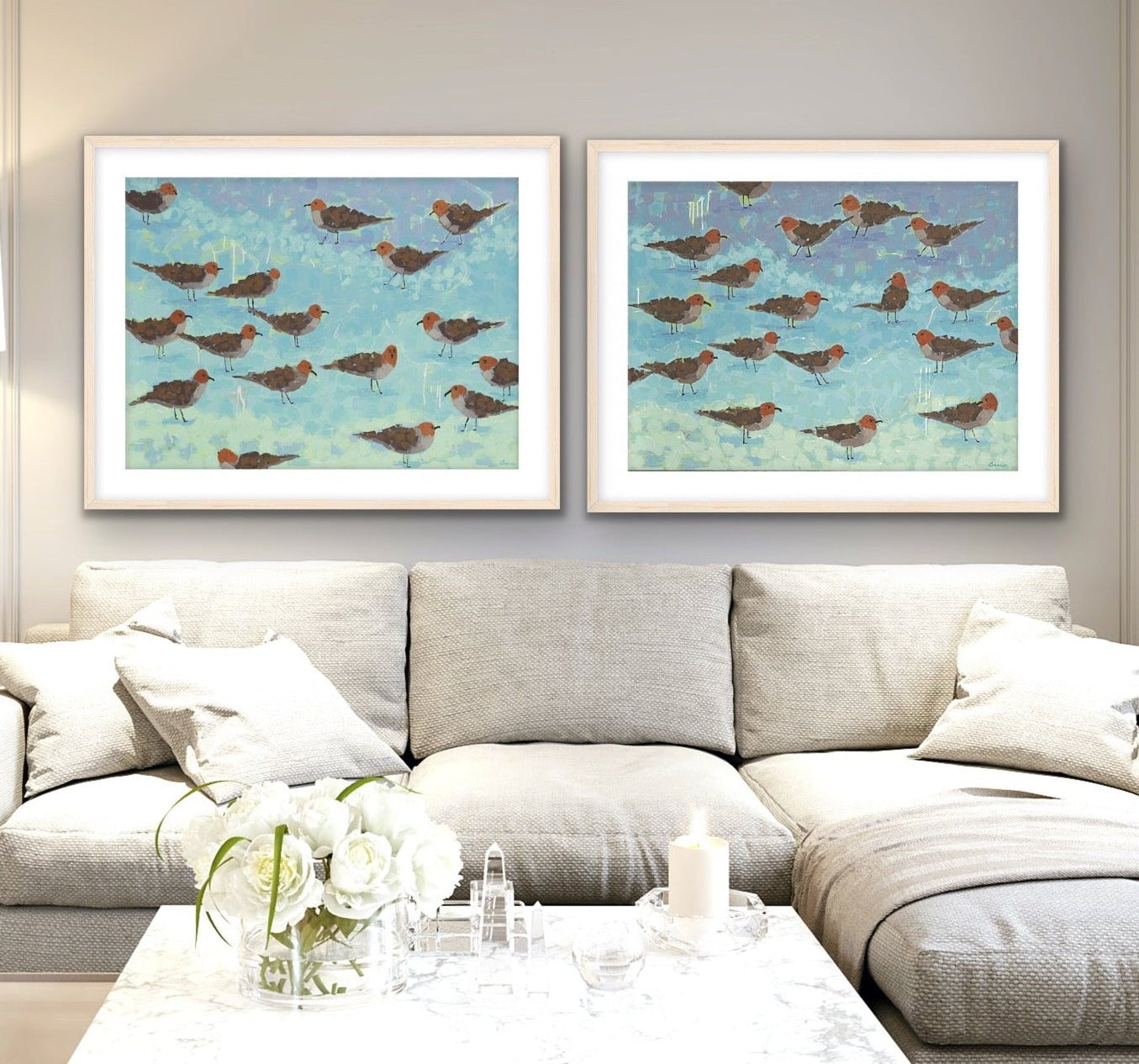 Morning Briefing I & II by Martha Brane – coastal fine art diptych featuring sandpipers along soft aqua and seafoam waters in a modern living room with a gray sectional sofa, and coffee table.
