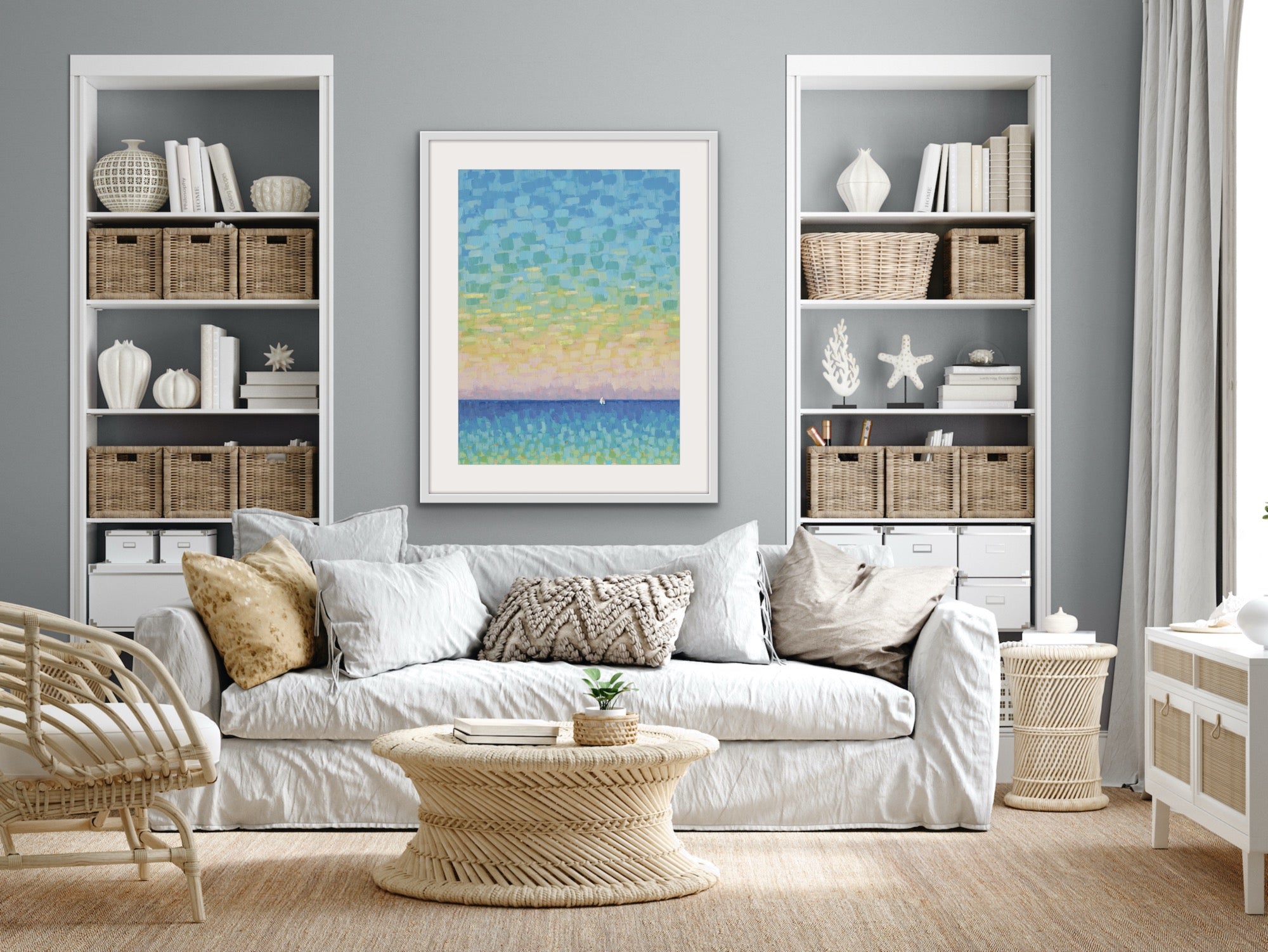 Living room with white sofa, wicker coffee table, bookshelves and a serene sailboat artwork matted and framed on the wall.