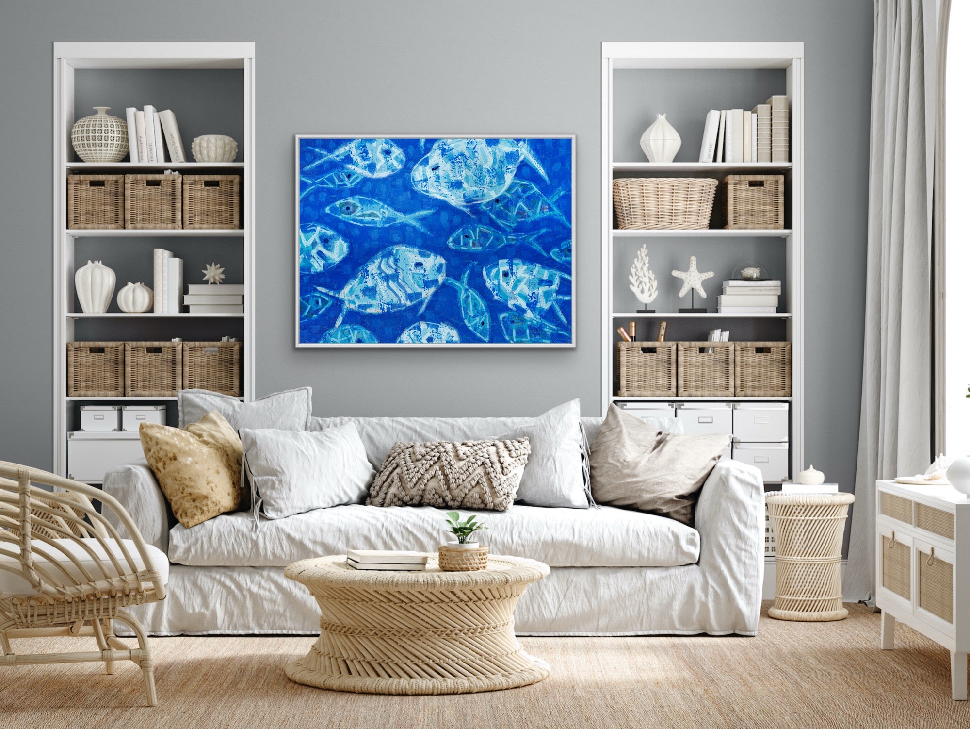 Living room with white sofa, wicker coffee table, and bookshelves with decorative items and a contemporary coastal wall art with shimmering blue fish on the wall.