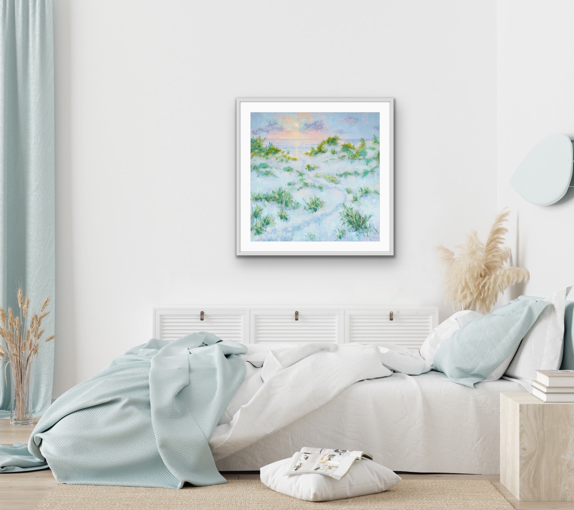 Framed  sunrise dune beach artwork above a bed in a bedroom with light blue bedding.