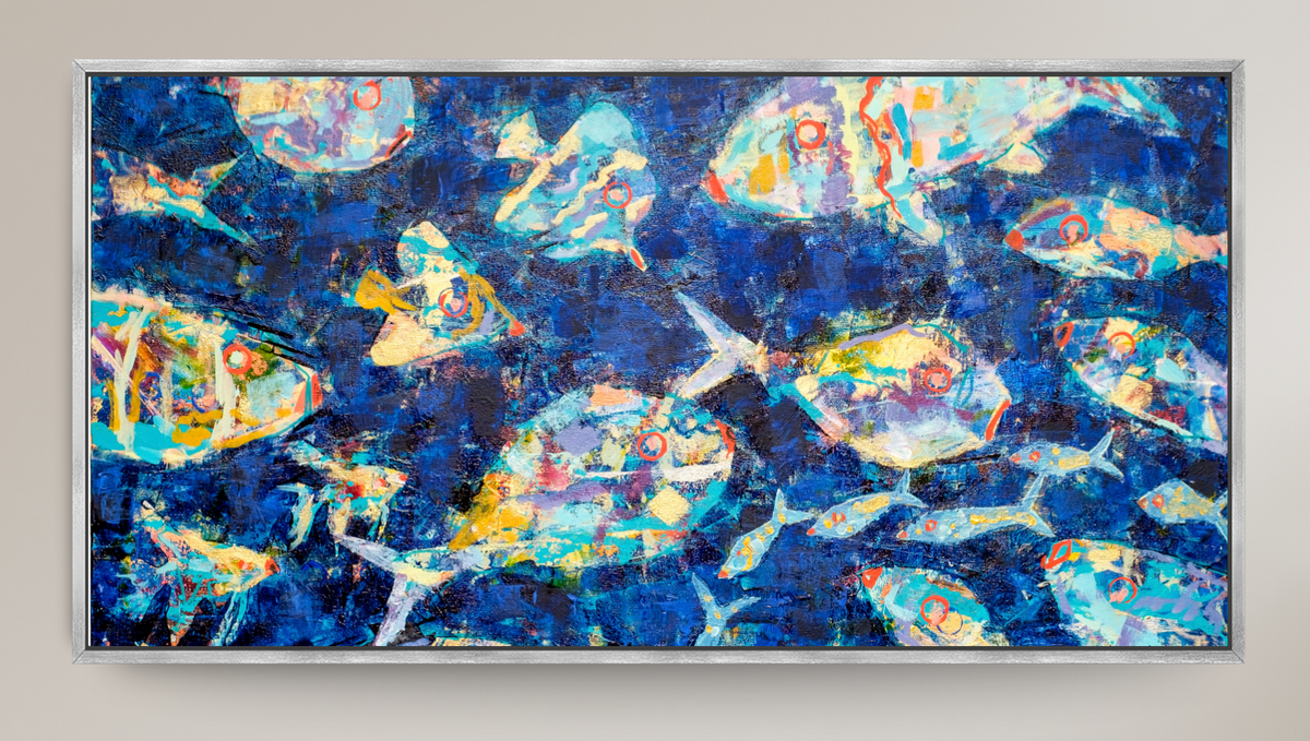 A framed square art print depicting stylized blue fish swimming underwater with bubbles, shown against a light beige wall.