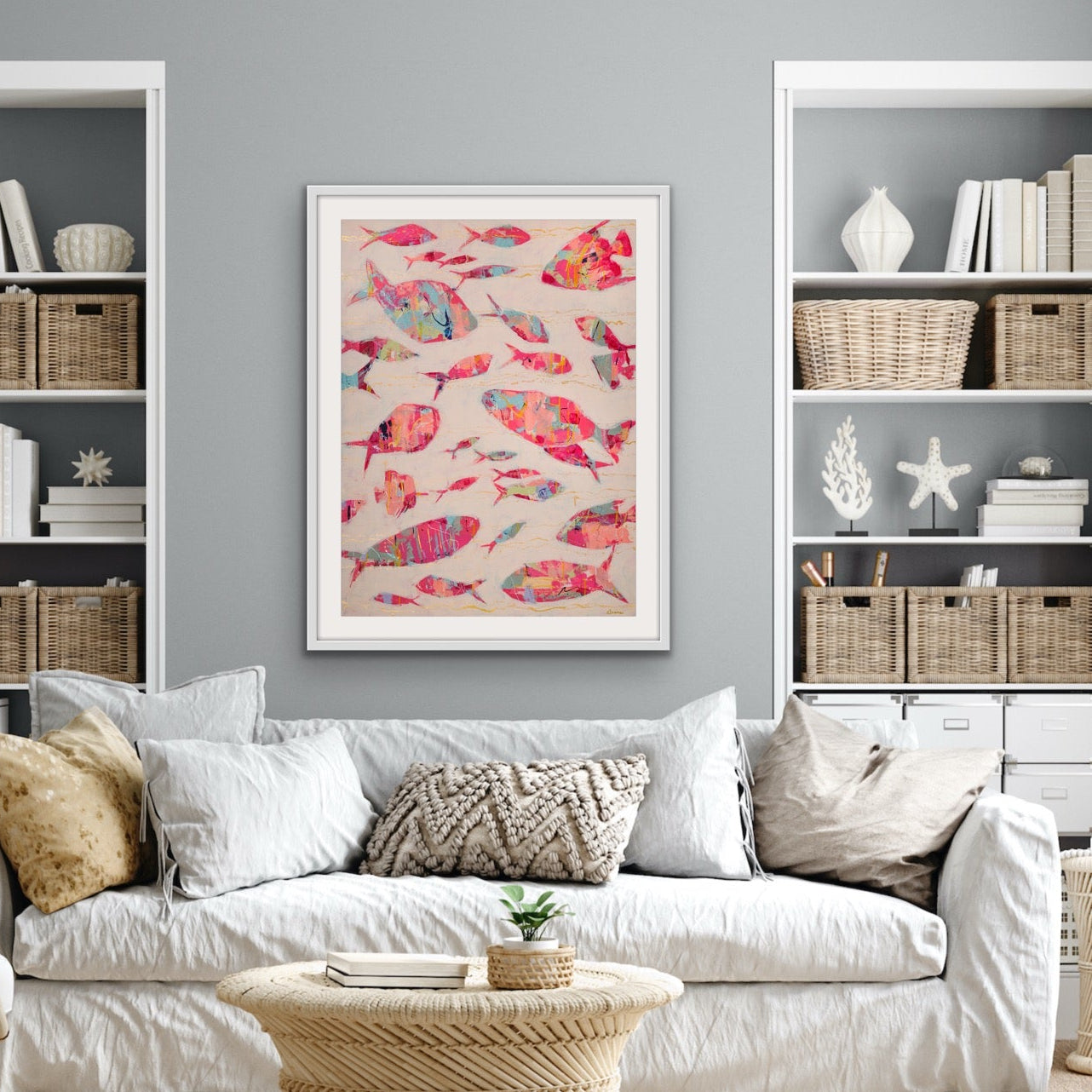 Contemporary seascape with colorful fish artwork in a Living room with white sofa, wicker coffee table, and bookshelves.