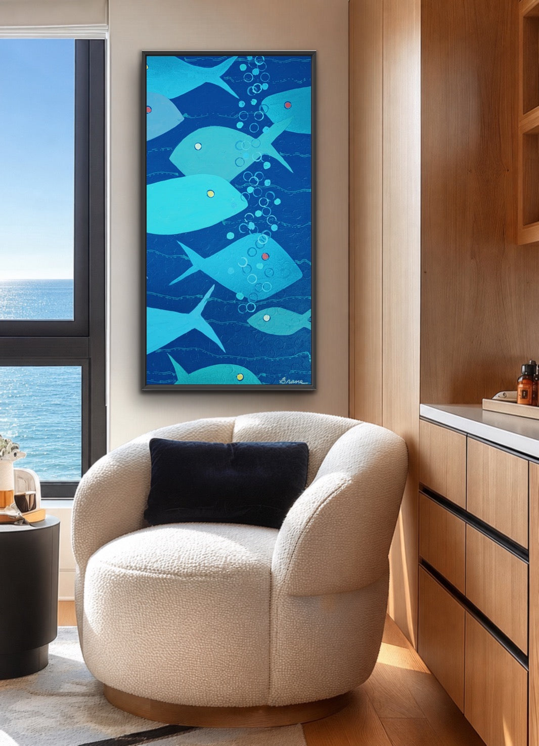 A framed vertical wall art print featuring stylized blue and turquoise fish swimming underwater with bubbles, displayed in a modern living room above a cream boucle armchair.